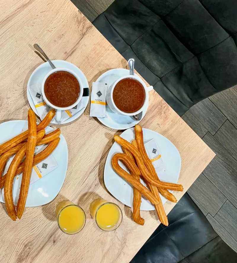Dos tazas de chocolate con churros y zumos de naranja sobre la mesa