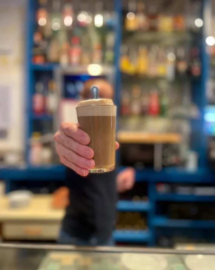 Un café con leche servido en vaso sobre la barra